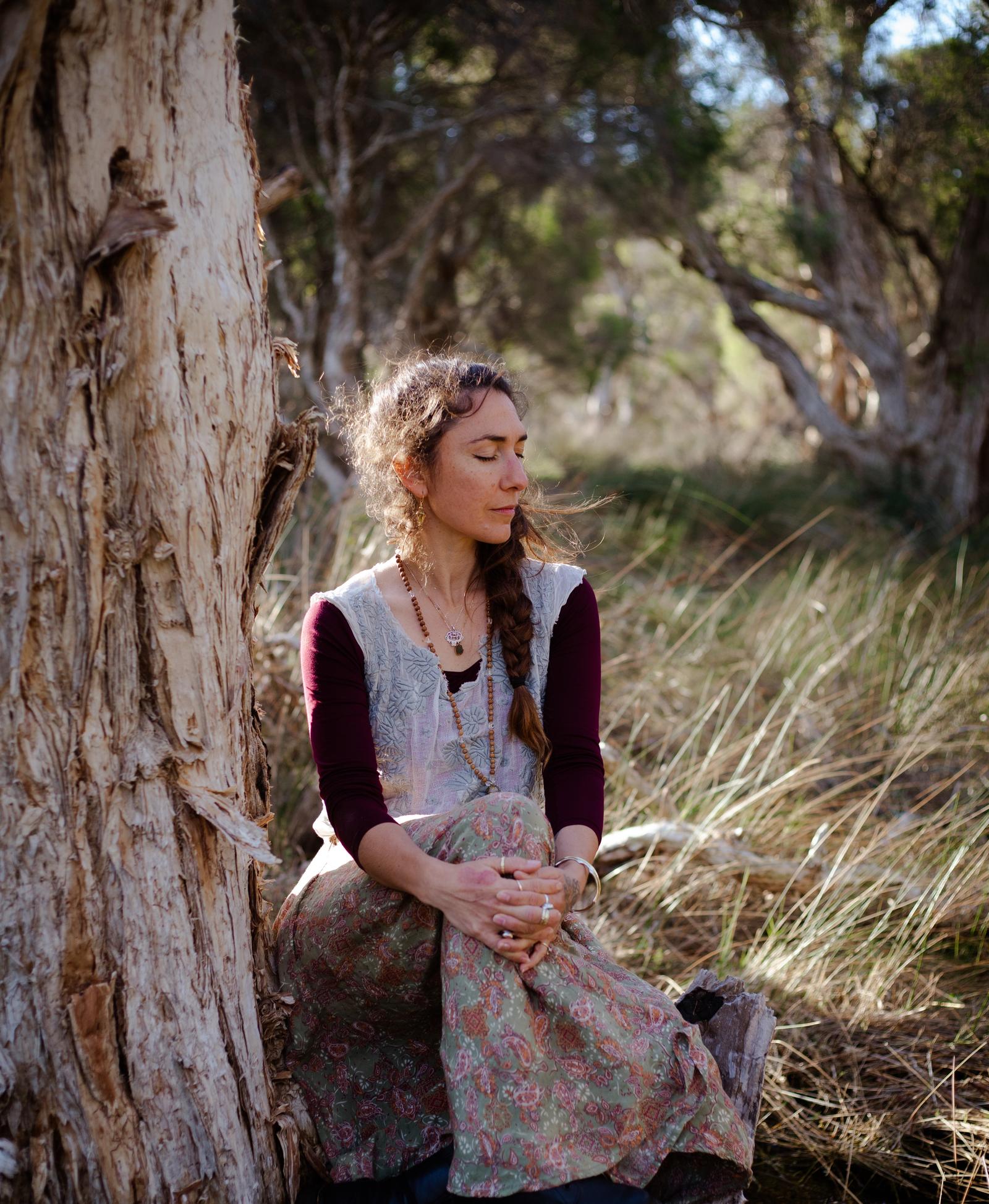 Priya meditating peacefully against a tree in nature, yoga and meditation teacher in South Fremantle
